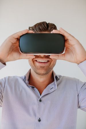 Shot of happy young man wearing virtual reality goggle against gray background