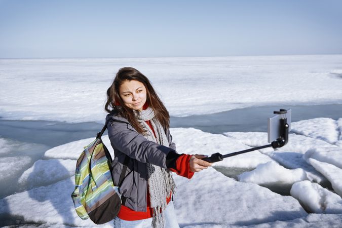 Female traveler outdoors at icy landscape using monopod to make