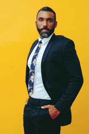 Content Black male in navy suit with floral tie in yellow studio
