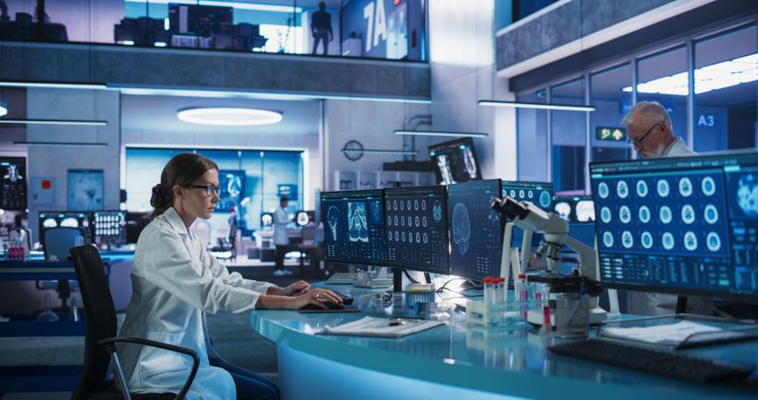 Diverse Colleagues Working In Medical Research Laboratory: Female Neurologist Analyzing CT Scans Of Human Brain On Desktop Computer.