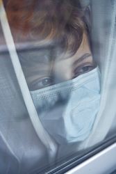 Crop boy in medical mask near window at home