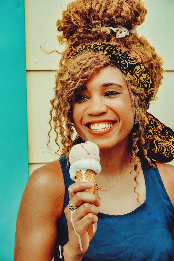 Vertical shot of happy Black female smiling with an ice cream cone in the sun