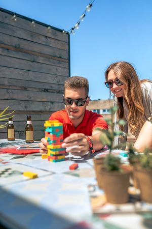 Concentrated young man pushing game piece next to female friend in rooftop party