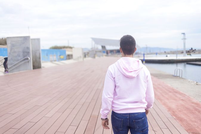 Back of male teenager walking on promenade along the water