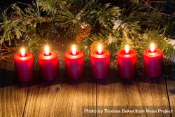 Glowing red candles with snow covered evergreen branch on wood 4Zo1Ob