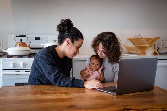 Woman on laptop at kitchen table with wife and baby