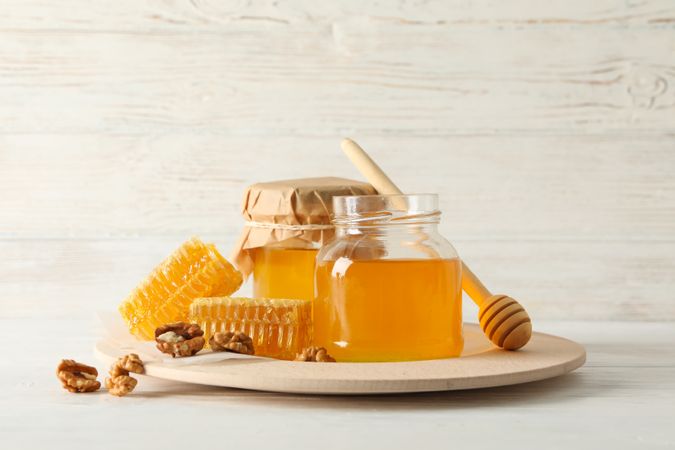 Honeycombs, walnuts, dipper and jars with honey on wooden background, copy space
