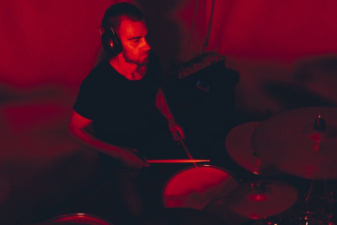 Man with drumsticks playing on drums in redness