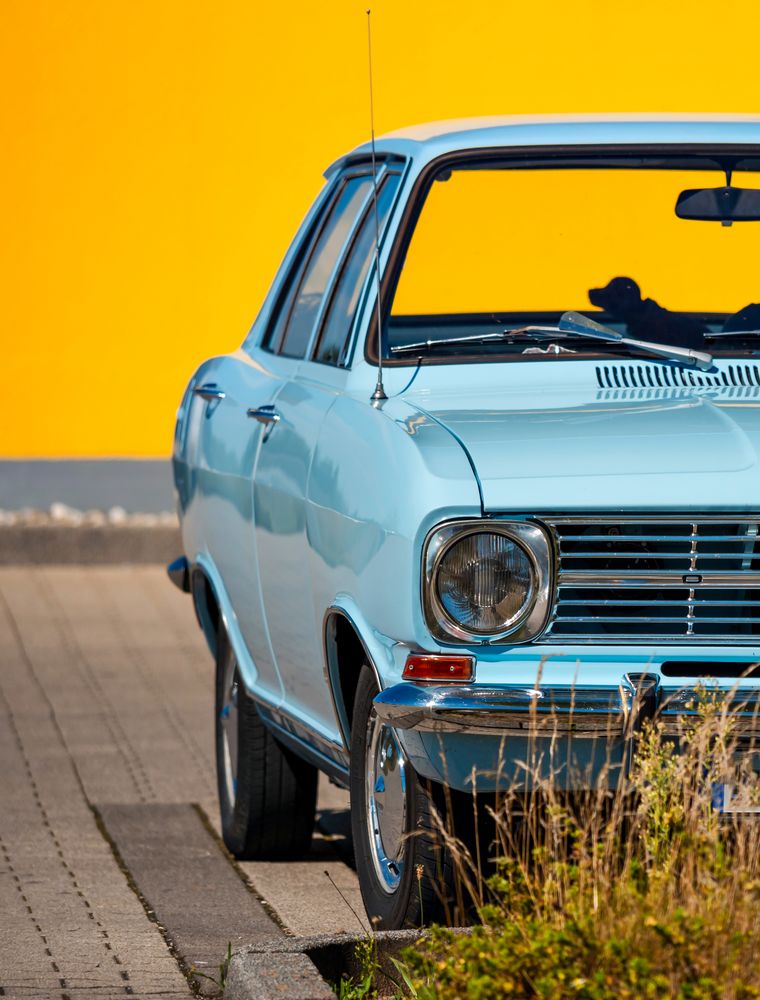 Sky blue retro car against a bright yellow wall. Color contrast.