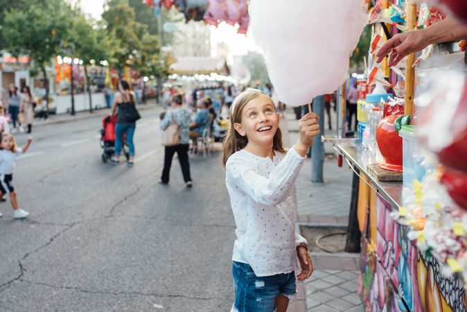Cheerful girl eating cotton candy on street