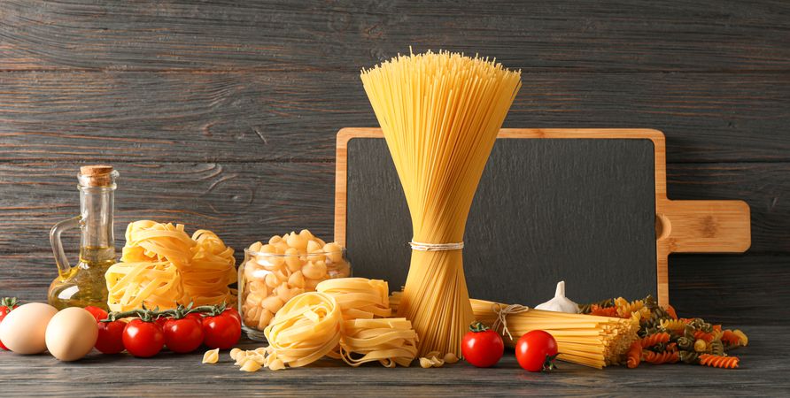 Composition with pasta cooking ingredients on wooden table, space for text