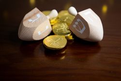 Close up of two tan wooden dreidels and golden gelt with menorah