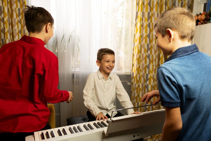 Smiling boy playing the piano while two friends watch