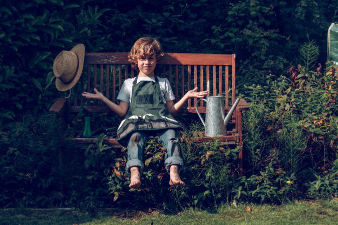 Kid in apron sitting on bench in garden