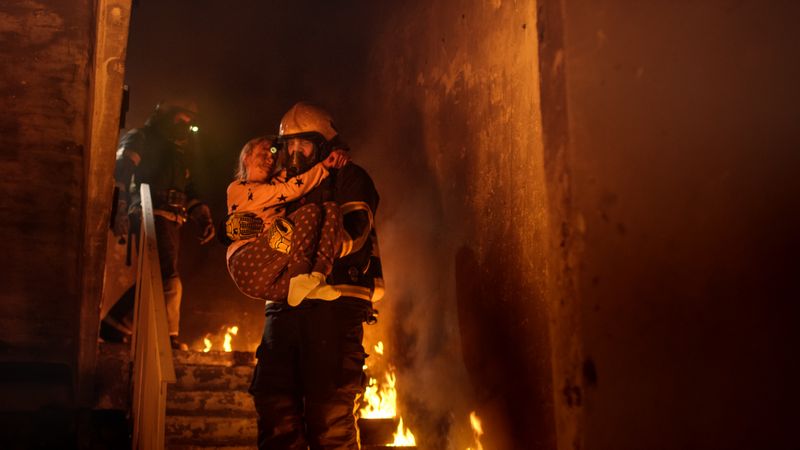 Brave fireman going down stairs of a burning building with a girl in his arms