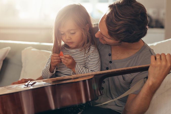 Man sitting with his daughter at home holding a guitar