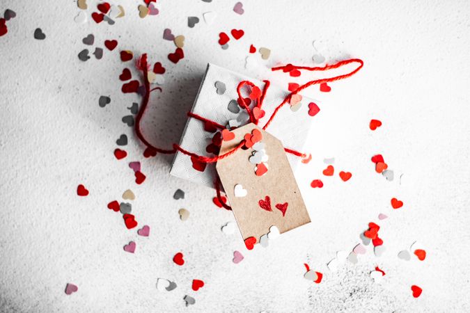 St. Valentine day concept with small gift wrapped in red ribbon and heart confetti