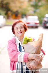 Older woman in pink cardigan holding grocery bag standing outdoor 5QX6d0