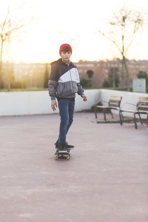 Teenager skateboarder riding on asphalt in playground at sunset