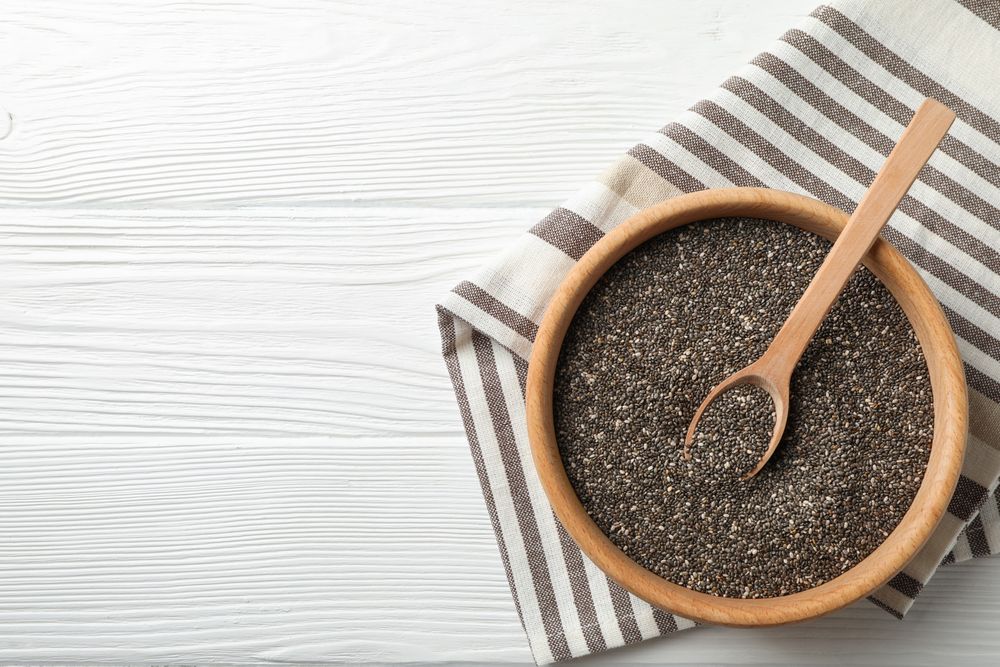 Wooden bowl with chia and spoon on wooden background, top view