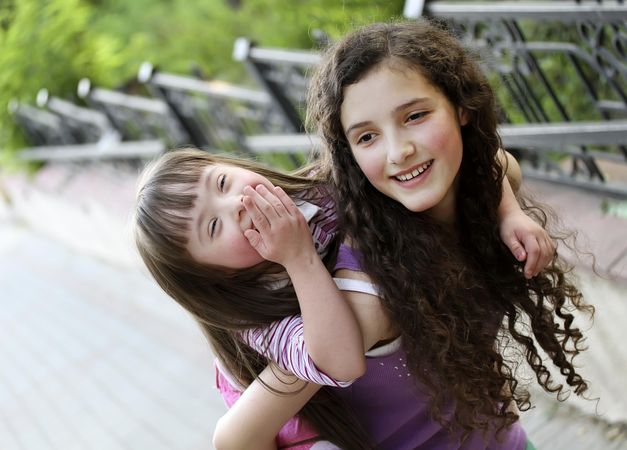 Big sister carrying her little sister in piggyback at the park