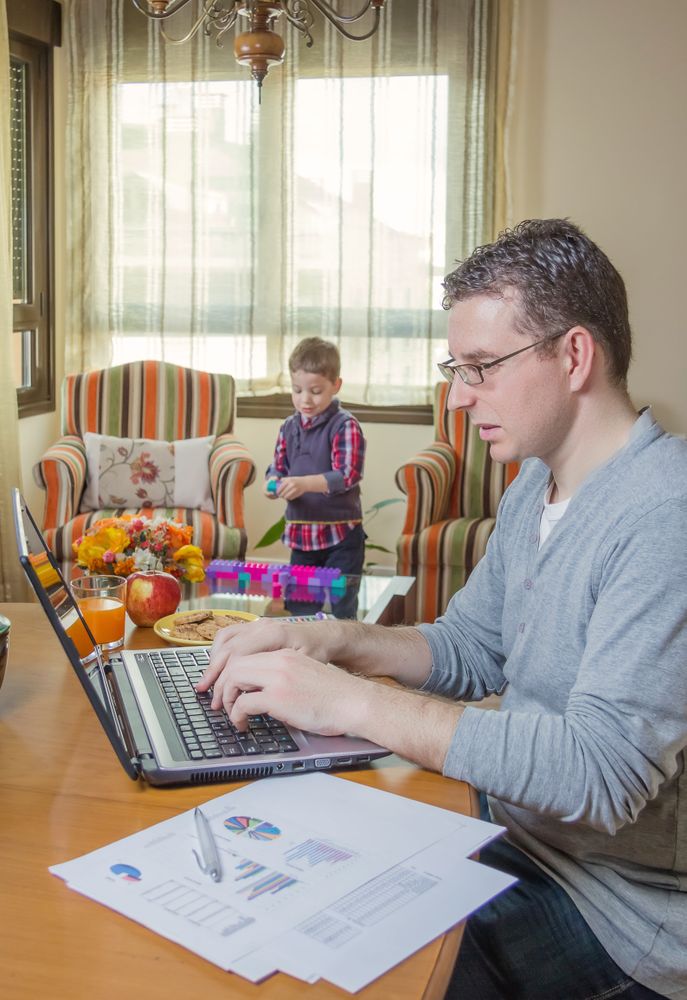 Father working in home office and son playing