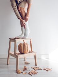 Crop female in socks on ladder with pumpkin