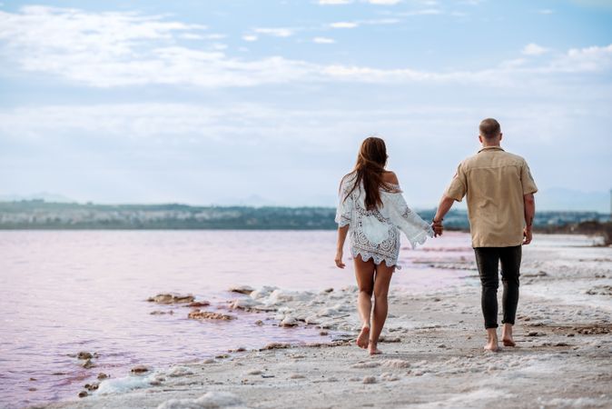 back view of adorable couple walking on an amazing beach with pink water