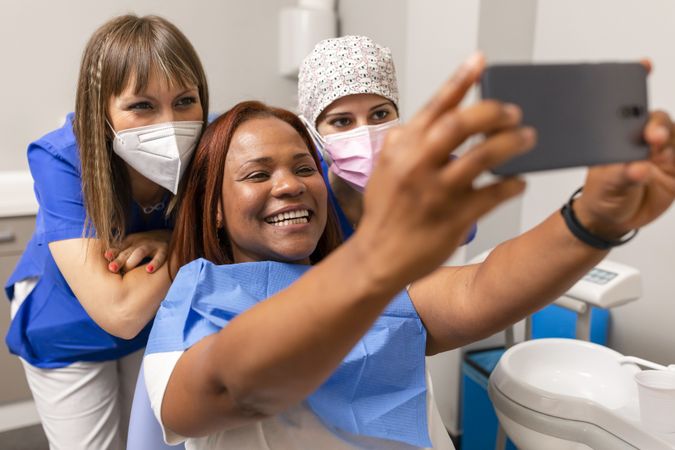 A Black woman patient, takes a happy selfie with dentist and dental hygienist at the clinic
