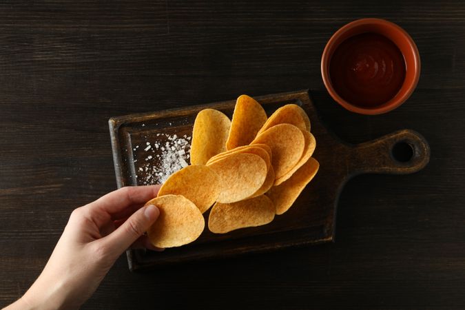 Potato chips on a wooden board with salt on a dark background