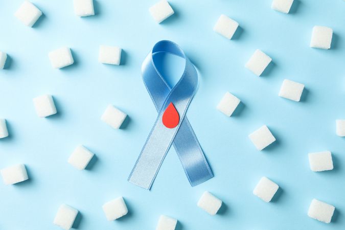 Diabetes awareness ribbon and sugar cubes on blue background