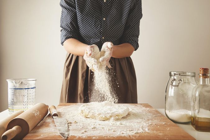 Woman adding flour to needed dough on breadboard
