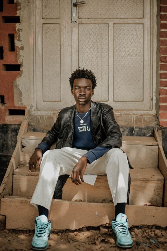 Young man in dark leather coat sitting on doorstep