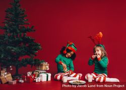Cute little girls wearing Christmas pajamas and hats eating cookies with milk 4B23k4