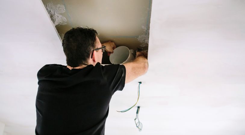 Man placing tube for kitchen hood installation on kitchen ceiling