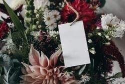 Closeup of blank paper card, gift tag label on colorful pink and burgundy dahlias, cosmos and aster flowers