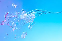Ice cubes and splash of water in vibrant bold gradient purple and blue holographic color lights