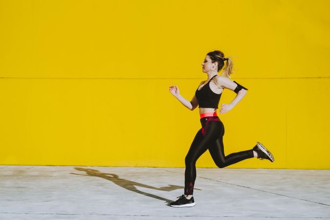 Woman with earphones running near wall