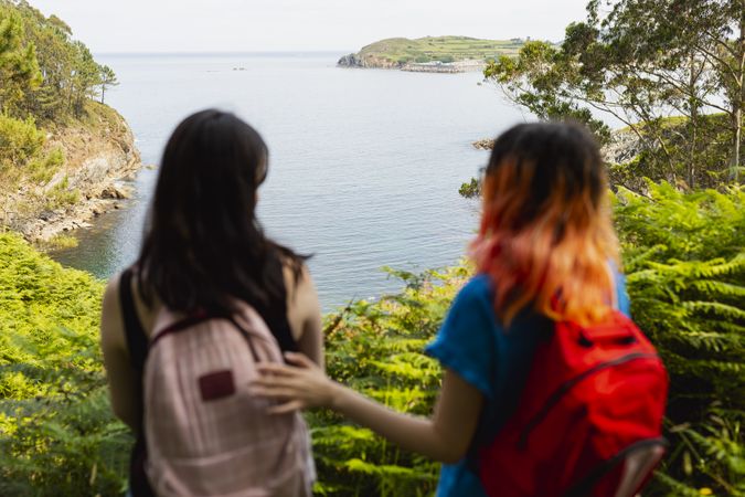 Two young people, out of focus in the foreground, enjoy a hike through the woods to a natural beachfront by the sea, focus in the background