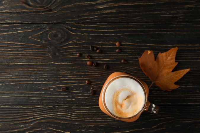 Glass jar of pumpkin latte, coffee seeds and leaf on wooden background