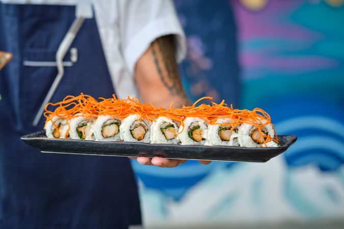 Crop chef with delicious uramaki sushi on marble tray