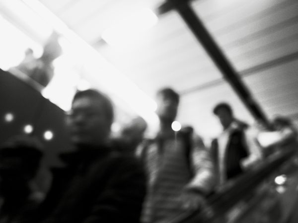 Blurry photo of men on escalator in grayscale