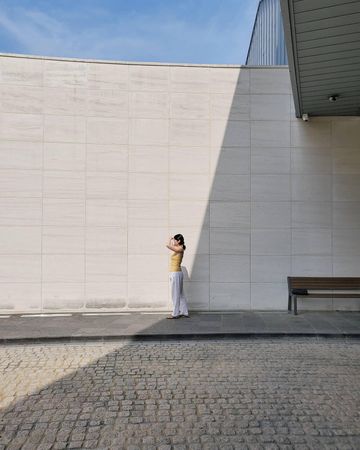 Woman standing on sidewalk beside light wall