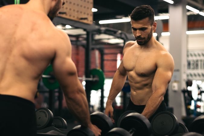 strong man standing in front of the mirror taking dumbbells in a gym