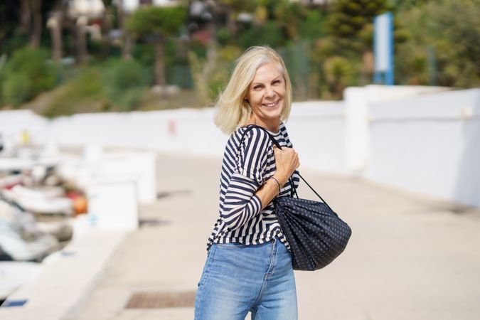 Happy older woman in jeans and striped shirt turning around outside on sunny day