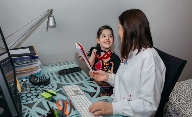 Woman teleworking with daughter showing her a drawing