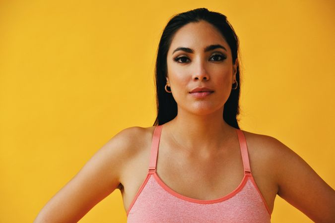 Hispanic woman in yoga clothes with hands on hips in yellow room, close up