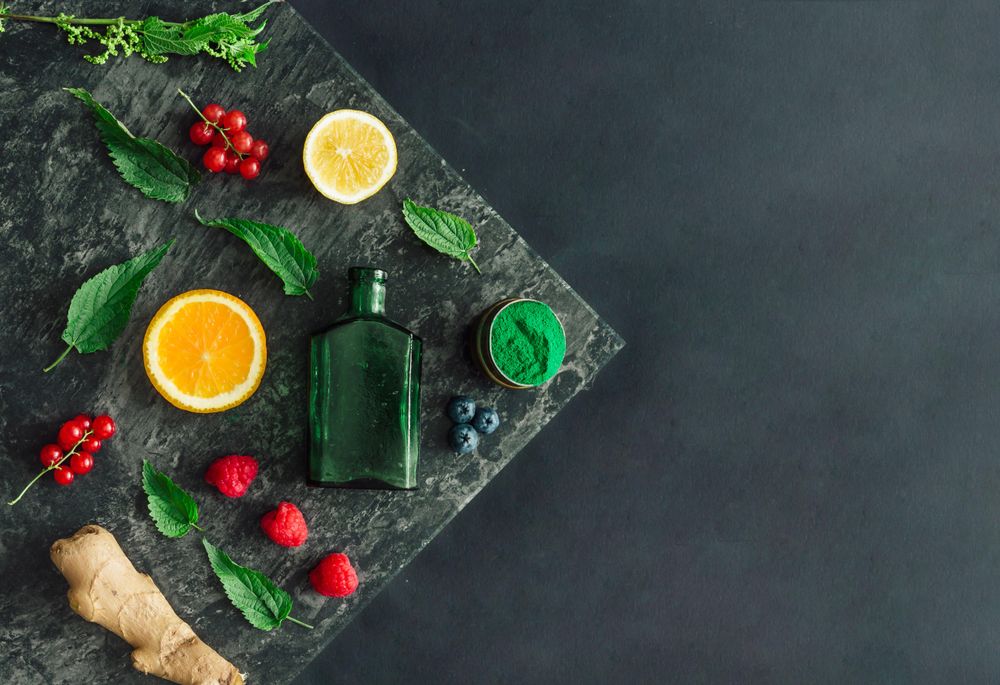 Healthy scene of spirulina powder, nettle leaves, berries, ginger on marble slap on dark background