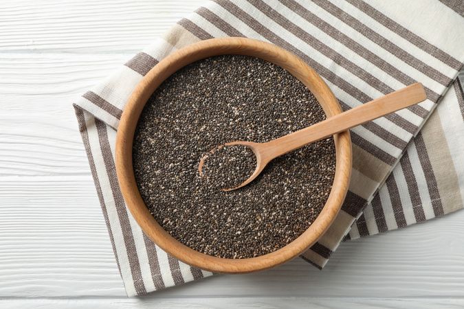Wooden bowl with chia and spoon on wooden background, top view