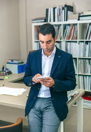 Businessman looking down at smartphone leaning on desk in office